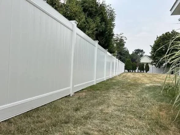 White vinyl privacy fence with posts and horizontal rails installed along residential property