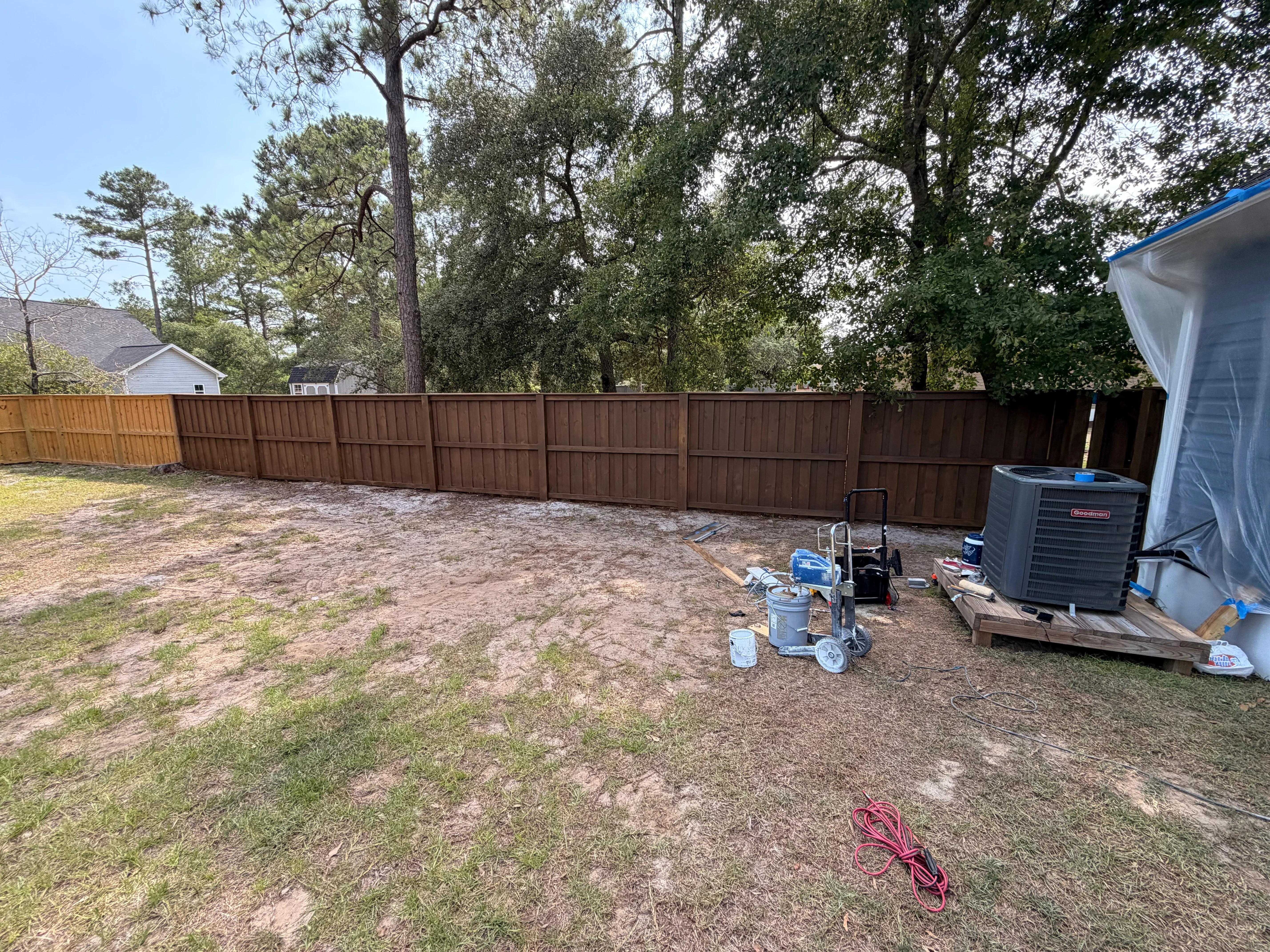 Brown vertical board wood privacy fence installed along backyard property line with mature trees