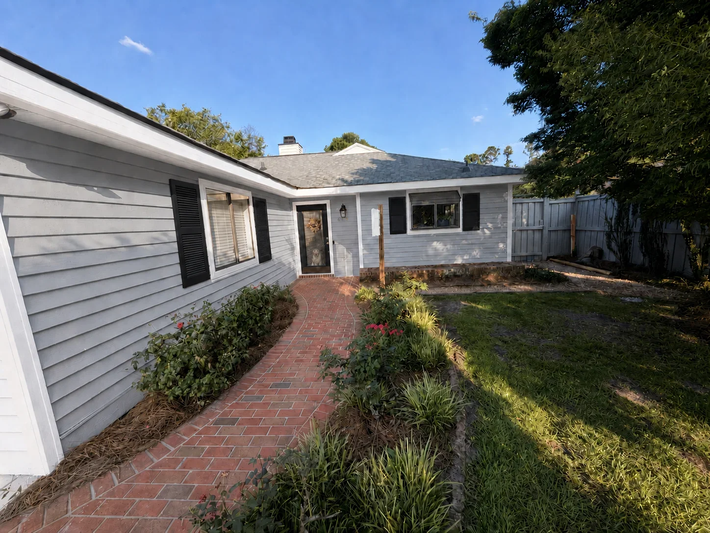 Gray vinyl siding house with black trim, red brick paver walkway, and wooden fence installation