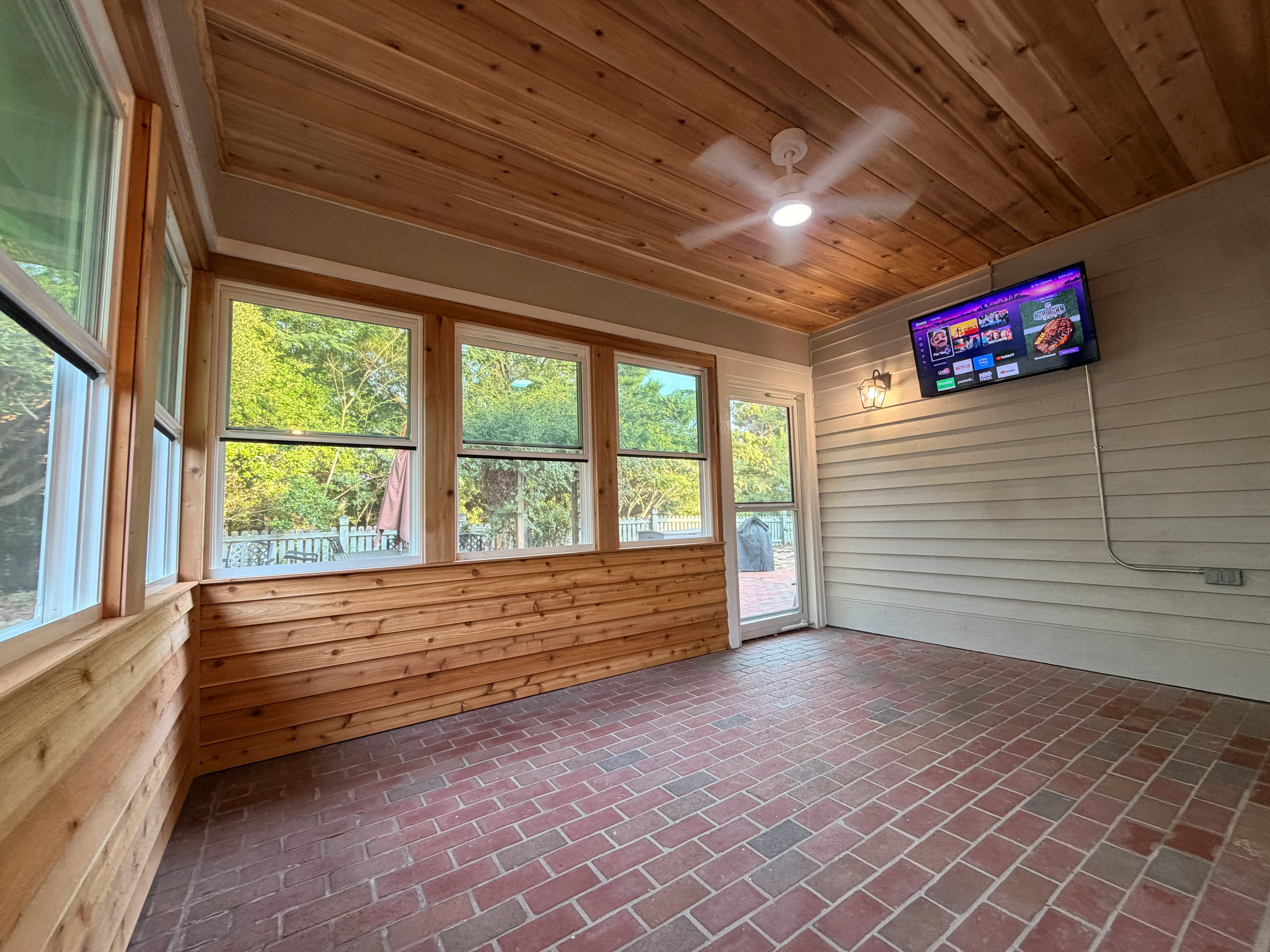 Screened porch with cedar wainscoting, horizontal siding, knotty pine ceiling, and brick flooring