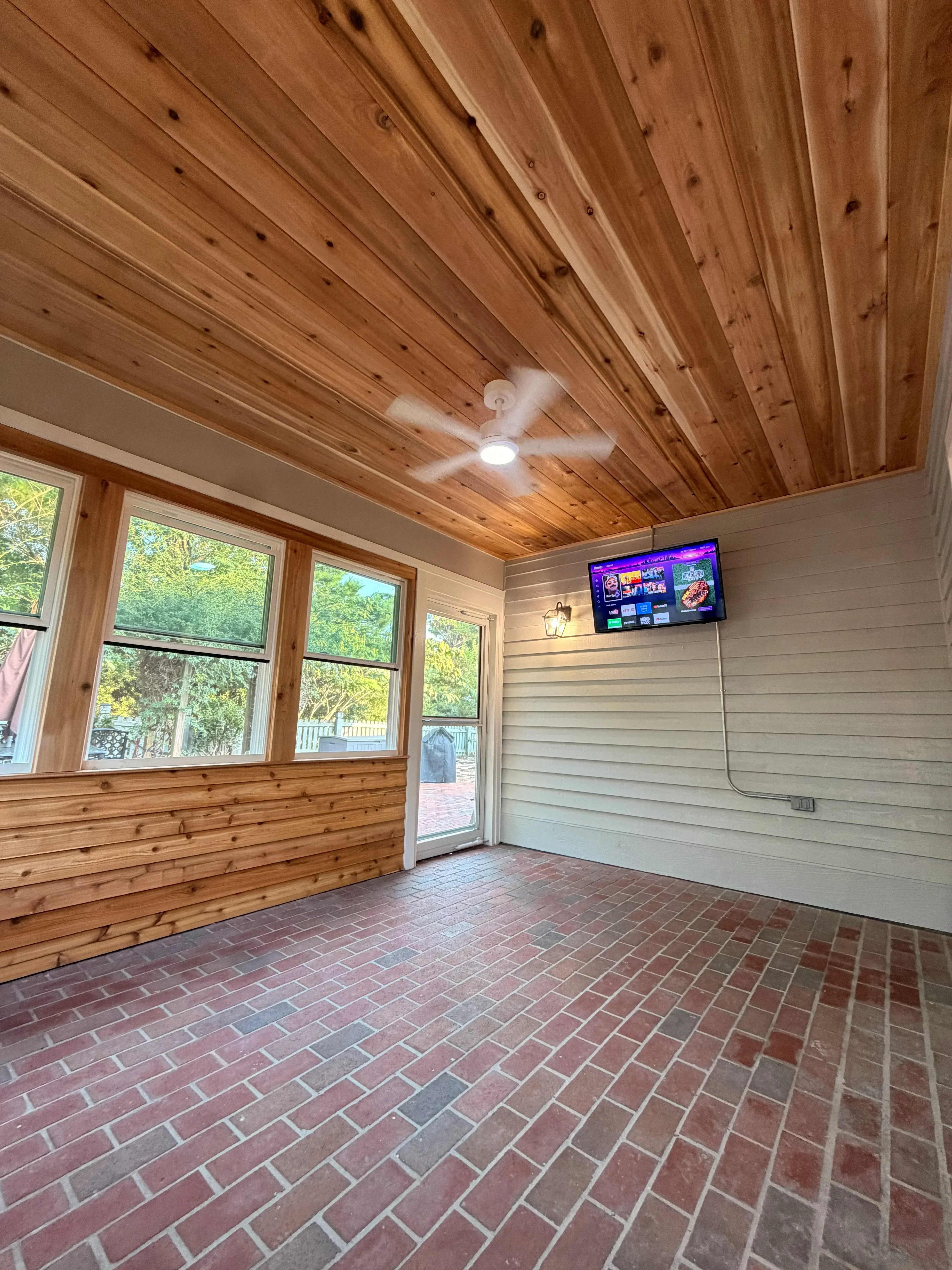 Cedar tongue-and-groove ceiling with white vinyl soffit, wood-framed windows, and ceiling fan installation