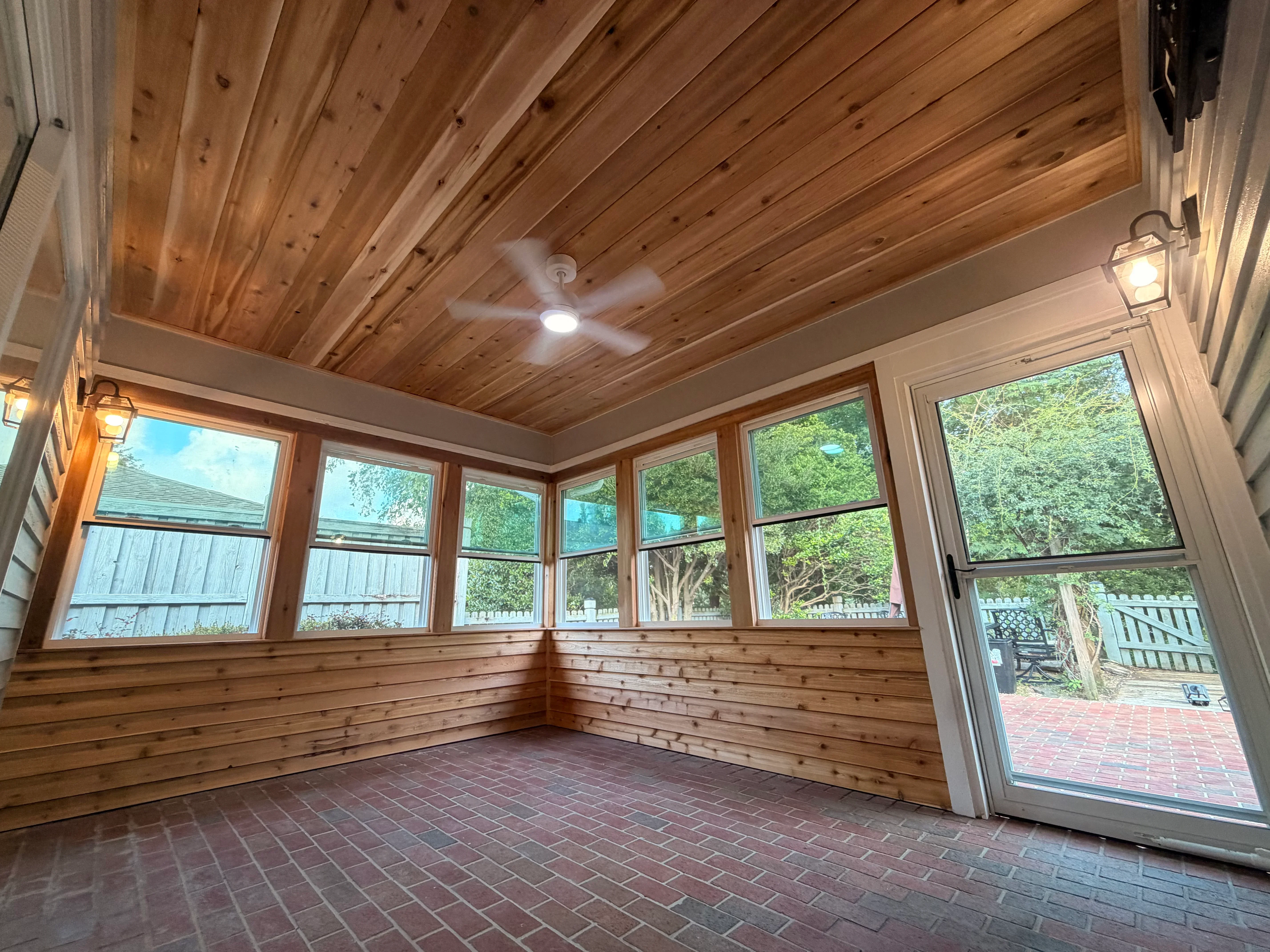 Cedar sunroom interior with vaulted wood ceiling, casement windows, and brick flooring