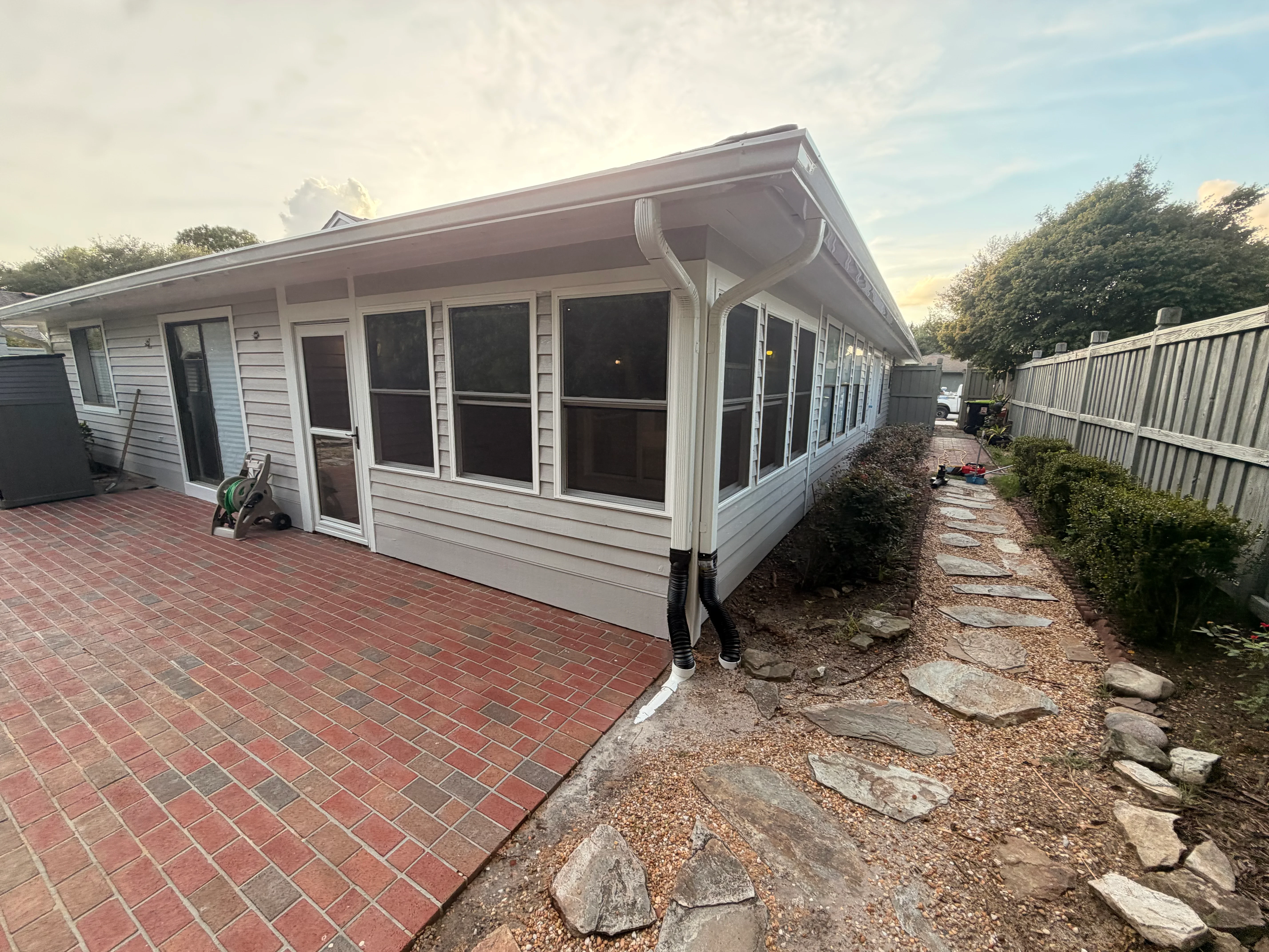 White vinyl sunroom with large windows, brick patio, and vinyl fence enclosure