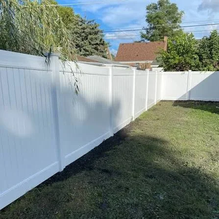 White vinyl privacy fence with vertical boards installed in residential backyard